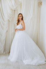 Fototapeta premium Beautiful girl in a white long luxurious wedding dress. Model bride posing in a gentle location