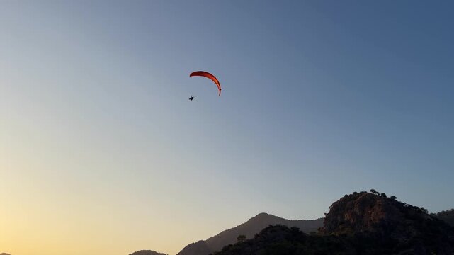 Paraglider flying over mountain landscape at sunset. Dynamic outdoor scene with clear sky, warm evening light, and a sense of freedom, adventure, and extreme sport travel. 