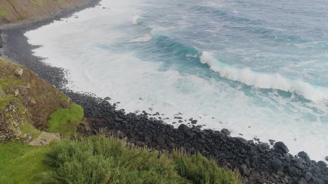 4K video; slow drone flight over the rocky northwest coast of the isle of Madeira; surf on a pebble beach