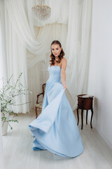 Fototapeta premium Portrait of a beautiful woman in a blue dress against a background of flowering plants and white elegant fabrics