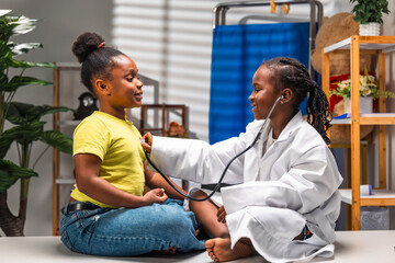Obraz premium African girl children role-playing doctor and patient with stethoscope during pediatric visit in clinic