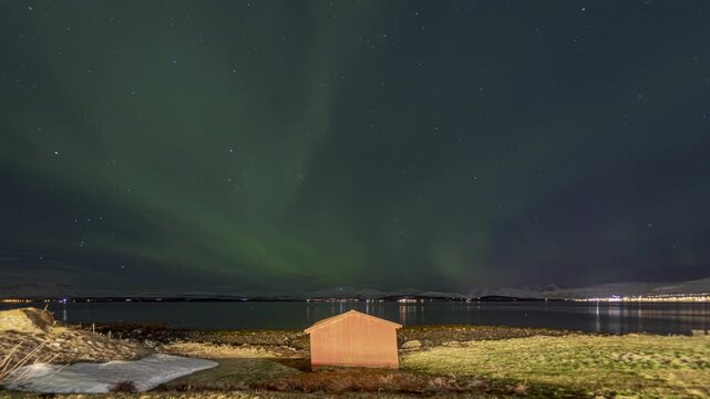 Cinematic 4K Timelapse of Northern Lights (Aurora Borealis) Dancing Over a Snowy Tromso Landscape With a Rustic Wooden Cabin Foreground