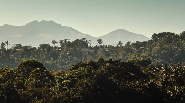 Aerial panorama of Lombok tropical island rainforest. Senaru mountains in hazy distance, rising above a dense canopy filled with lush green trees and scattered village homes. Indonesia landscape