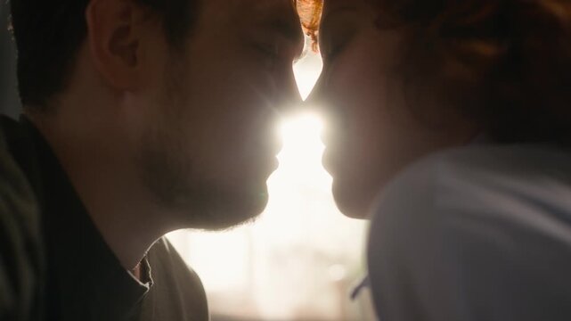 Cinematic close up shot of happy young couple cuddling affectionately and touching noses in sunlight enjoying intimate moment at home