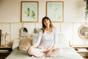 Woman relaxing at home, sitting on bed, smiling