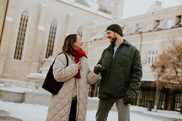 Korean woman and Caucasian man walk and talk in a snowy city area on a winter day