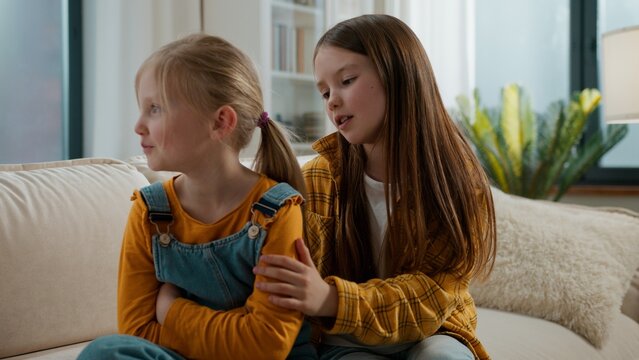 Two Caucasian kids sisters quarrel problem little younger girl pretending offended laughing smiling pretend ignoring older sister talking apologizing sorry talk cute sisters siblings children at home