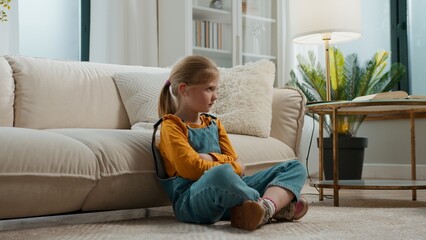Irritated stressed frustrated Caucasian little kid girl child daughter breathing hard feeling sad offended breath sitting on floor at home near couch childhood problem family adoption custody trouble