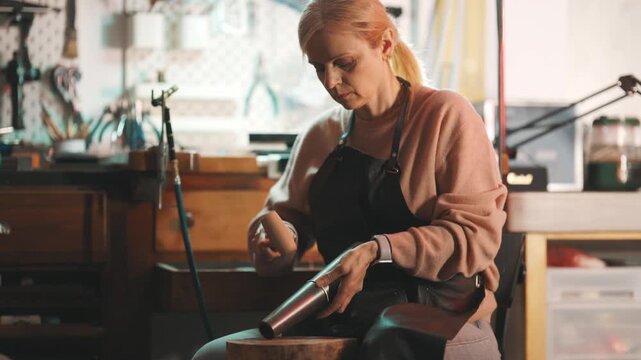 Female artisan shaping metal with a mallet in her workshop