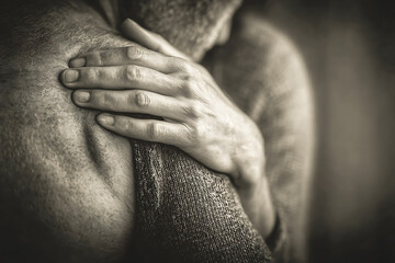 A monochrome close-up of a hand resting on a person&rsquo;s bare back, capturing an intimate, emotional moment with strong texture and soft light.