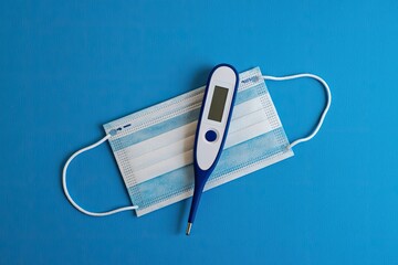 Medical face mask and digital thermometer on blue background