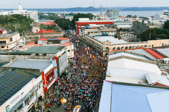 Aerial view of a bustling street filled with a vibrant crowd, framed by colonial buildings and a distant coastline, Iloilo City, Western Visayas, Philippines.