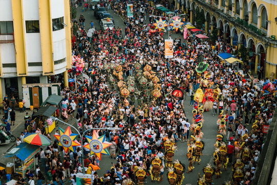 Aerial view of a jubilant street parade with crowds lining heritage buildings under the sun, Calle Real visible in the background, Iloilo City, Western Visayas, Philippines.
