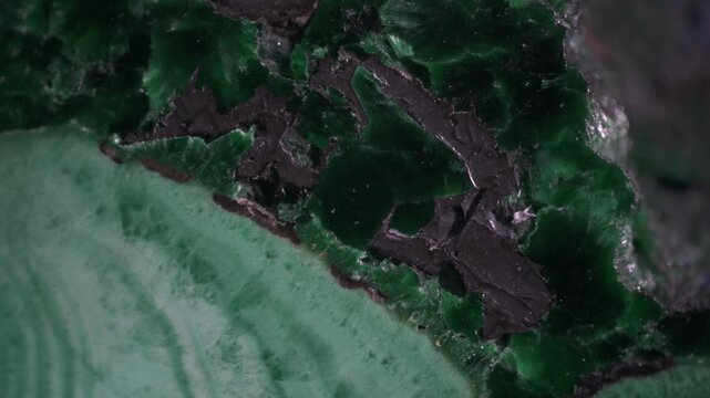 Macro video of polished malachite specimen from Kamenushinskoe deposit. Banded green zones, black inclusions and reflective surface under directional lighting