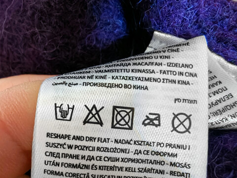 Close up of the care label with washing symbols icons. clothes label with cleaning instructions. Soft purple fabric. Hand wash only
