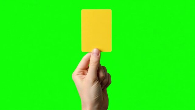 Hand holds yellow card on green screen background Penalty concept