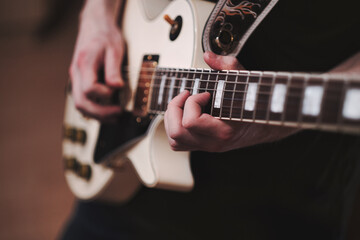 Obraz premium Close-up of hands playing electric guitar in warm studio light. Rock music performance with focus on rhythm, strings and expressive sound.
