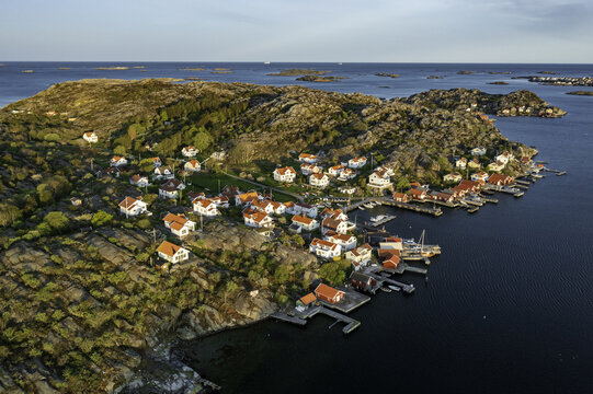 Aerial view of red-roofed houses clustered along the rocky shoreline, blending with the rugged landscape and deep blue waters, &Atilde;&hellip;stol, V&Atilde;&curren;stra G&Atilde;&para;taland County, Sweden.