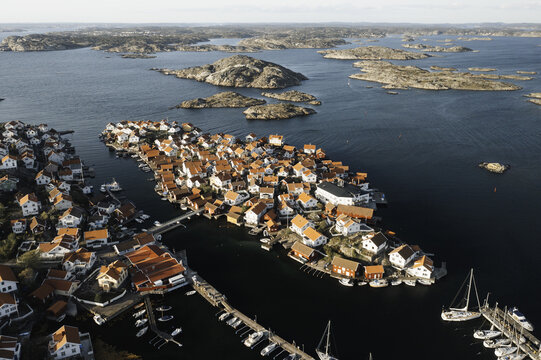 Aerial view of red-roofed houses cluster tightly on the island, contrasting with the deep blue sea and rocky outcrops, Gullholmen, V&Atilde;&curren;stra G&Atilde;&para;taland County, Sweden.
