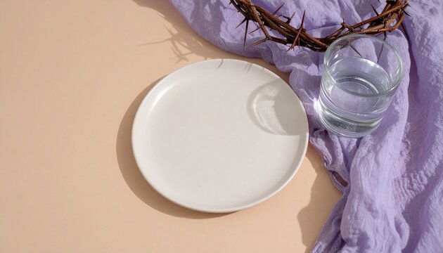 Fastenzeit &ndash; Leerer Teller mit Wasser und Dornenkranz auf violettem Tuch als Symbol f&uuml;r christliches Fasten und Verzicht