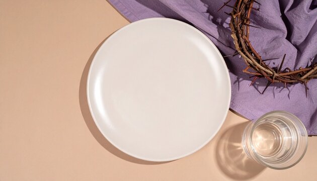 Fastenzeit &ndash; Leerer Teller mit Dornenkranz und Wasser auf violettem Tuch als Symbol f&uuml;r christlichen Verzicht