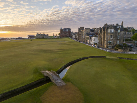Aerial view of the iconic Swilcan Bridge across the burn on the lush, green Old Course, touched by the warm glow of the setting sun, St Andrews, Scotland, United Kingdom.