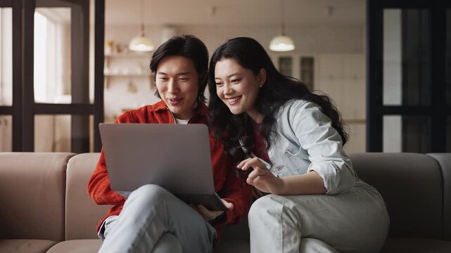 Smiling Korean couple choosing apartment to rent using laptop at home