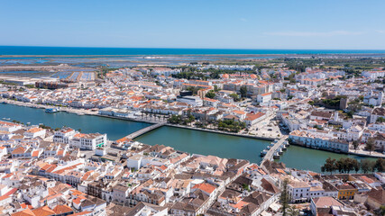 Obraz premium Tavira is shown from above with rivers, white buildings, and the Algarve coast visible. The sunny weather highlights the layout of the town and landscape. River Gilao Roman bridge