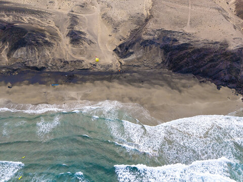 Aerial view of the dramatic coastline where the rugged cliffs meet the sandy shore and turquoise waves crash, Playa de la Pared, Fuerteventura, Spain.