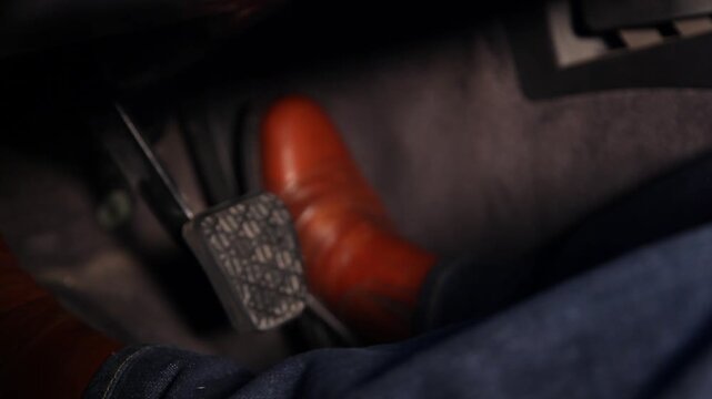 Close up view of a man's legs and feet wearing brown leather shoes and blue jeans while driving a car and pressing the brake and accelerator pedals.