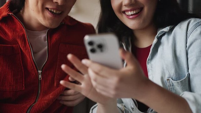 Happy Korean couple shopping online using phone, choosing stylish outfit