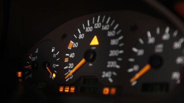 Close up view of a car dashboard instrument cluster focusing on the tachometer with the needle moving up and down as the engine revs, speedometer visible in background.

