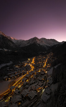 Aerial view of a village nestled among snow-capped mountains, lights twinkling against the dusky sky, a scene of serene beauty, Champ&Atilde;&copy;ry, Valais, Switzerland.