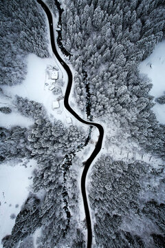 Aerial view of a winding road cutting through a snow-covered forest, creating a stark contrast between the dark asphalt and the pristine white landscape, Champ&Atilde;&copy;ry, Valais, Switzerland.