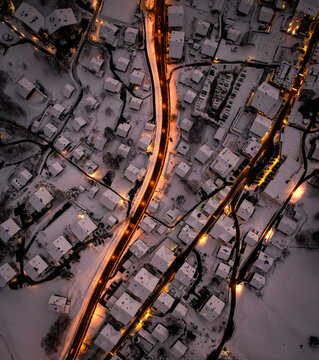 Aerial view of snow-blanketed roofs glisten under the soft glow of streetlights, casting long shadows across the quiet village, Champ&Atilde;&copy;ry, Valais, Switzerland.