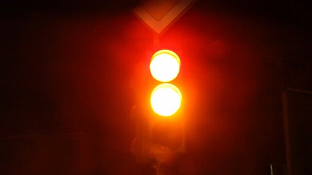 Close up low angle view of a traffic semaphore at night changing from red to yellow and finally green, signaling drivers to proceed on the dark street.

