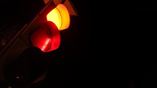 Close up low angle view of a traffic semaphore at night changing from red to yellow and finally green, signaling drivers to proceed on the dark street.

