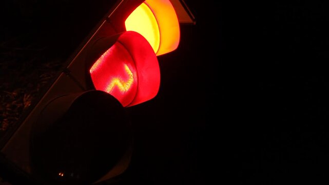 Close up low angle view of a traffic semaphore at night changing from red to yellow and finally green, signaling drivers to proceed on the dark street.

