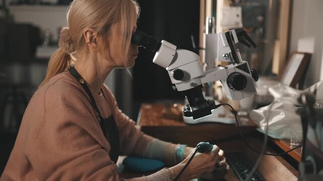 Woman working on jewelry with microscope in workshop