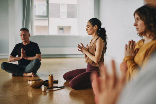 Female yoga instructor leading a group of students through a guided meditation during a class together on the floor of her studio