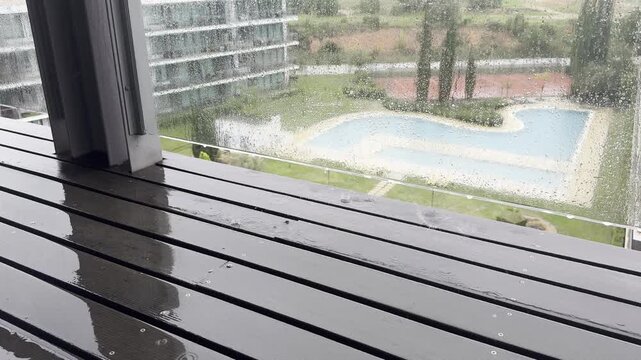 Balcony view of a rainy landscape with a pool and trees