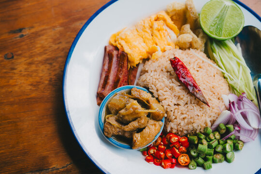 Kao kluk kapi Thai food. Fried rice with chili pepper and side dishes on white plate with blue rim on wooden table