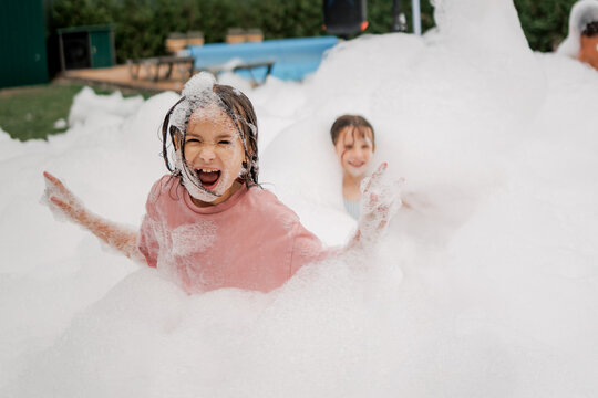 Kids laugh and play in huge foam pit outdoors on sunny day enjoying messy fun together