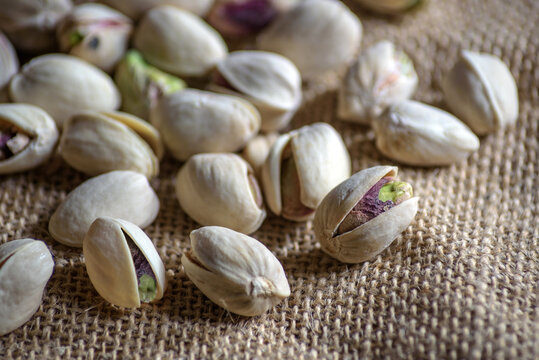 Primer plano de pistachos secos con c&aacute;scara (Pistacia vera) sobre fondo de saco r&uacute;stica de yute con enfoque selectivo. Imagen ideal para conceptos de alimentaci&oacute;n saludable.