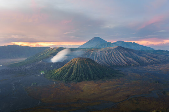 Aerial view of the majestic Mount Bromo, its volcanic cone breathing soft plumes against the dawn's pastel hues, East Java, Indonesia.