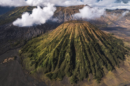 Aerial view of the majestic Mount Bromo and Batok volcanoes rise in a symphony of textures, where the golden slopes meet the dark, rugged terrain, Bromo, East Java, Indonesia.