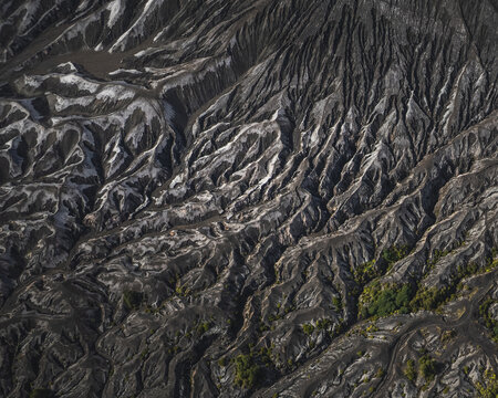 Aerial view of dramatic volcanic landscape, etched with deep ravines and stark contrasts of light and shadow, creating a textured tapestry of nature's raw power, Probolinggo, East Java, Indonesia.