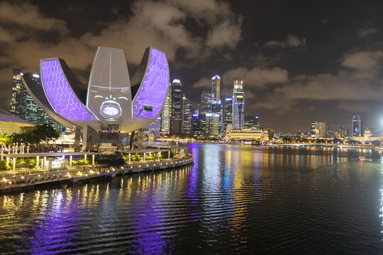 View of the illuminated ArtScience Museum casts a vibrant purple glow across the waters of Marina Bay, against the Singapore skyline, Singapore, Singapore.