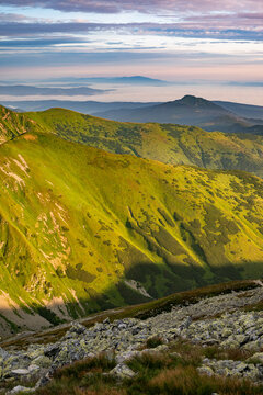 View of sunlight and shadows paint the rocky slopes leading to green mountain peaks, with distant hills fading into the misty horizon, Western Tatras, Zilina Region, Slovakia.