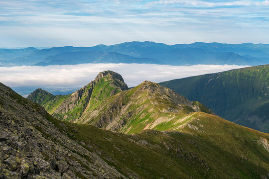 View of jagged mountain peaks pierce through a sea of clouds under a vast sky, blending rugged terrain with ethereal beauty, Jakubina, Zilina Region, Slovakia.